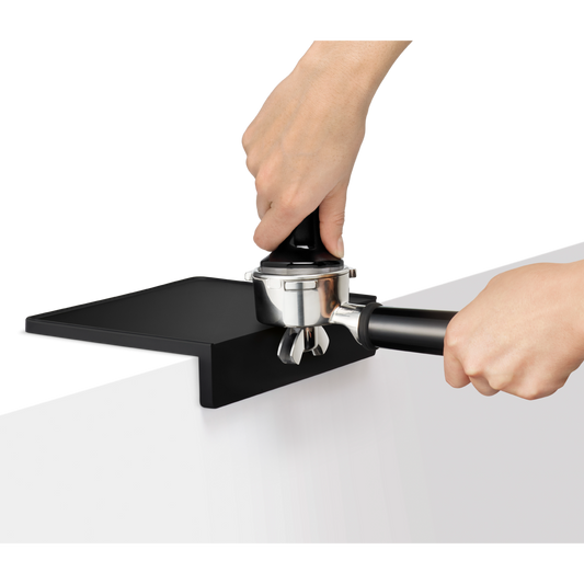 Person using a black and silver coffee tamping device on a white surface