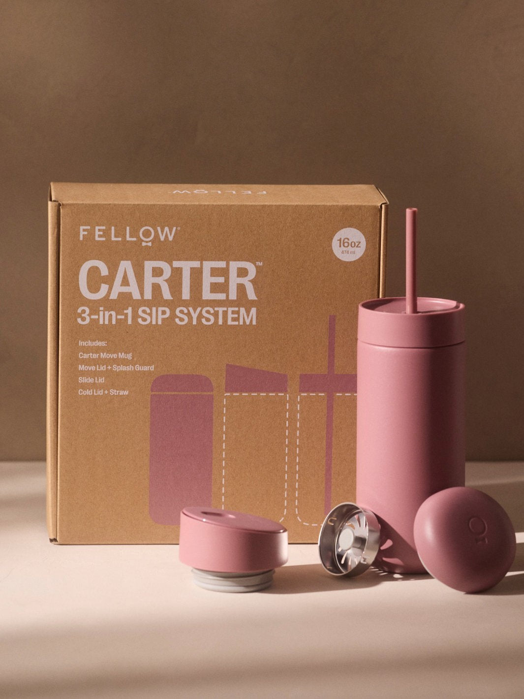 Fellow Carter 3-in-1 sip system with pink tumbler, lid, and straw on a brown background