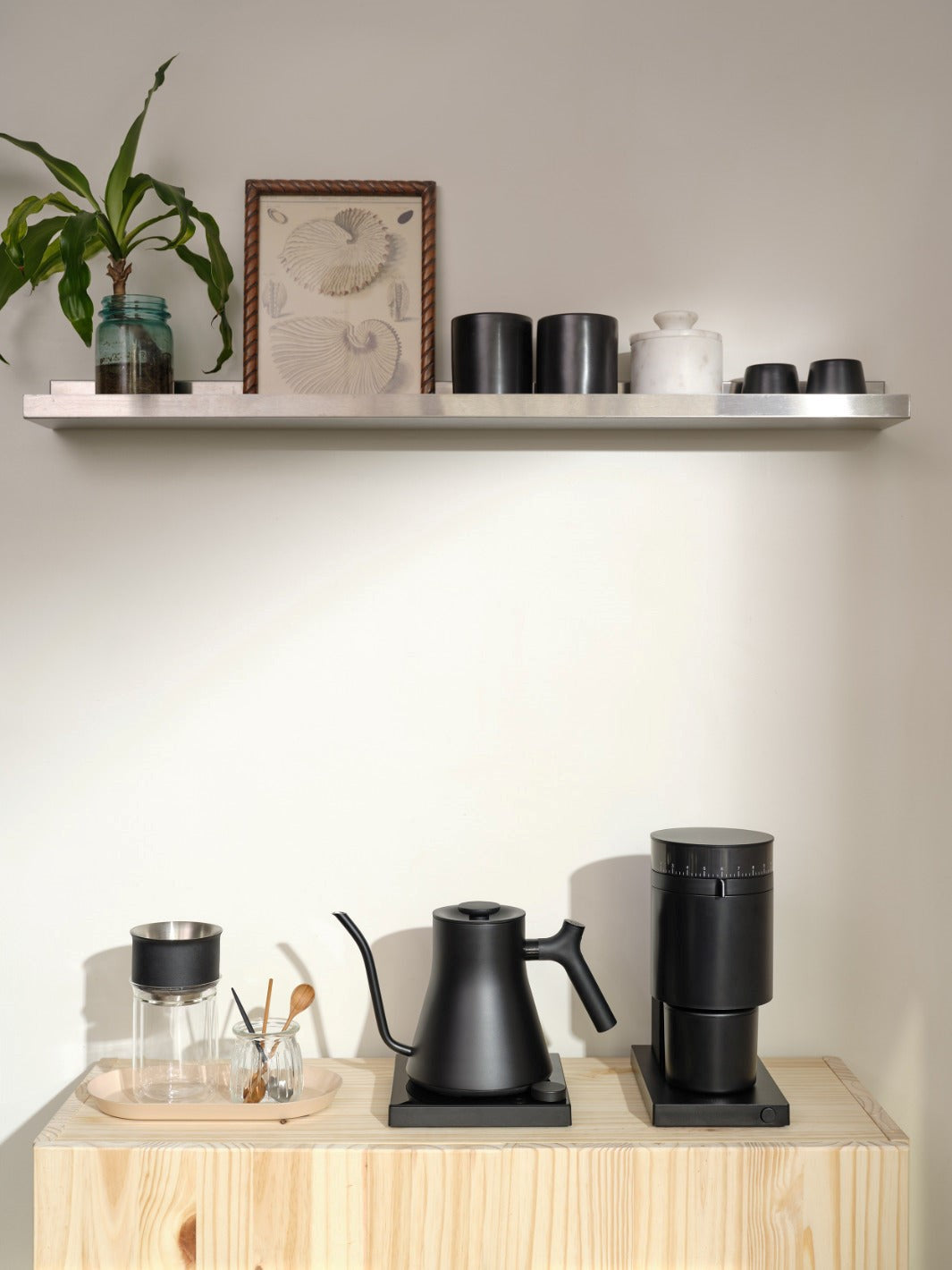 Black Fellow Stagg Gooseneck Kettle with Black Fellow Opus Coffee Grinder on a wooden surface with a shelf in the background.