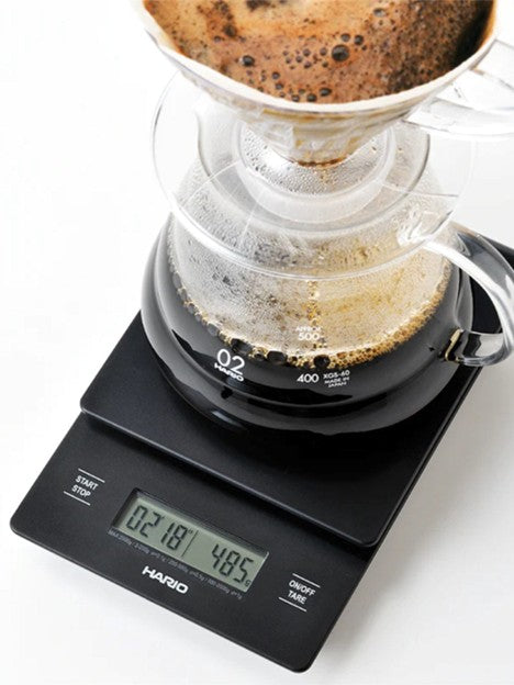 Coffee brewing process with a Hario digital scale measuring water and coffee grounds.