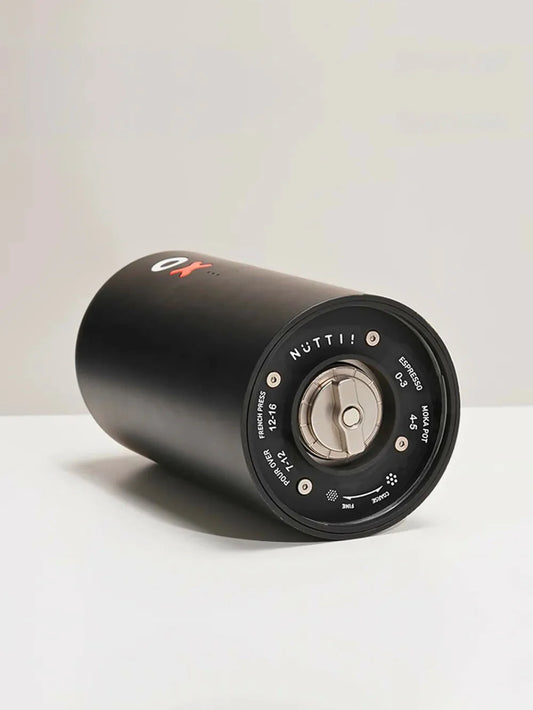 Black cylindrical coffee grinder with adjustment dial displayed with white writing and metal dial on a white background.