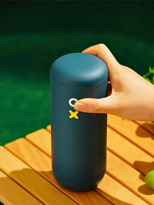 Blue coffee grinder with a white start button and yellow stop button, held by a hand on a wooden surface with a green background