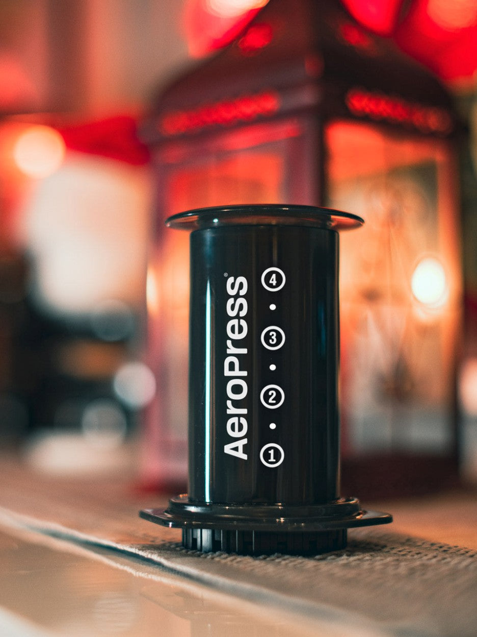 Black Aeropress coffee maker on a bar with blurred background