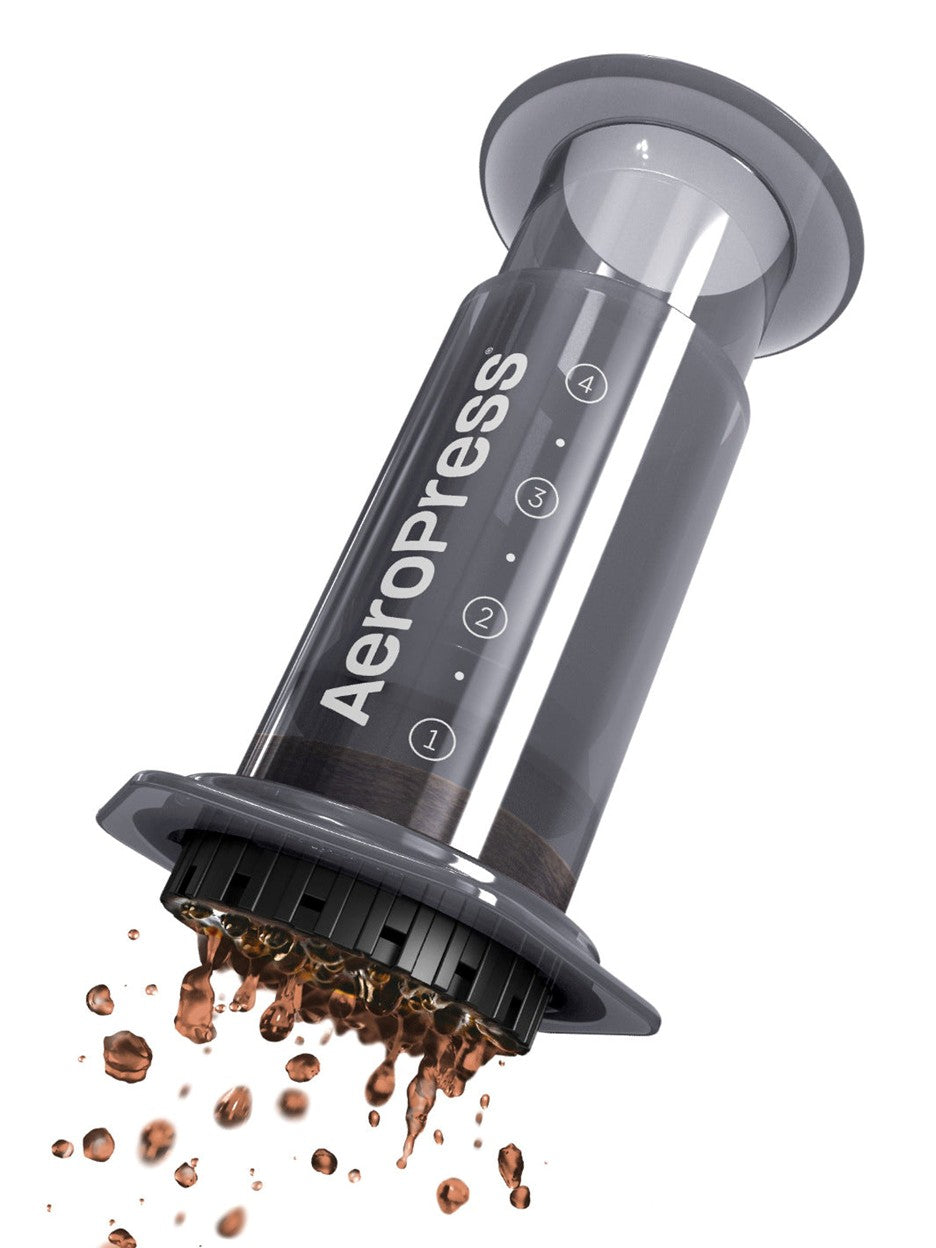 Aeropress coffee maker with coffee grounds spilling out on a white background