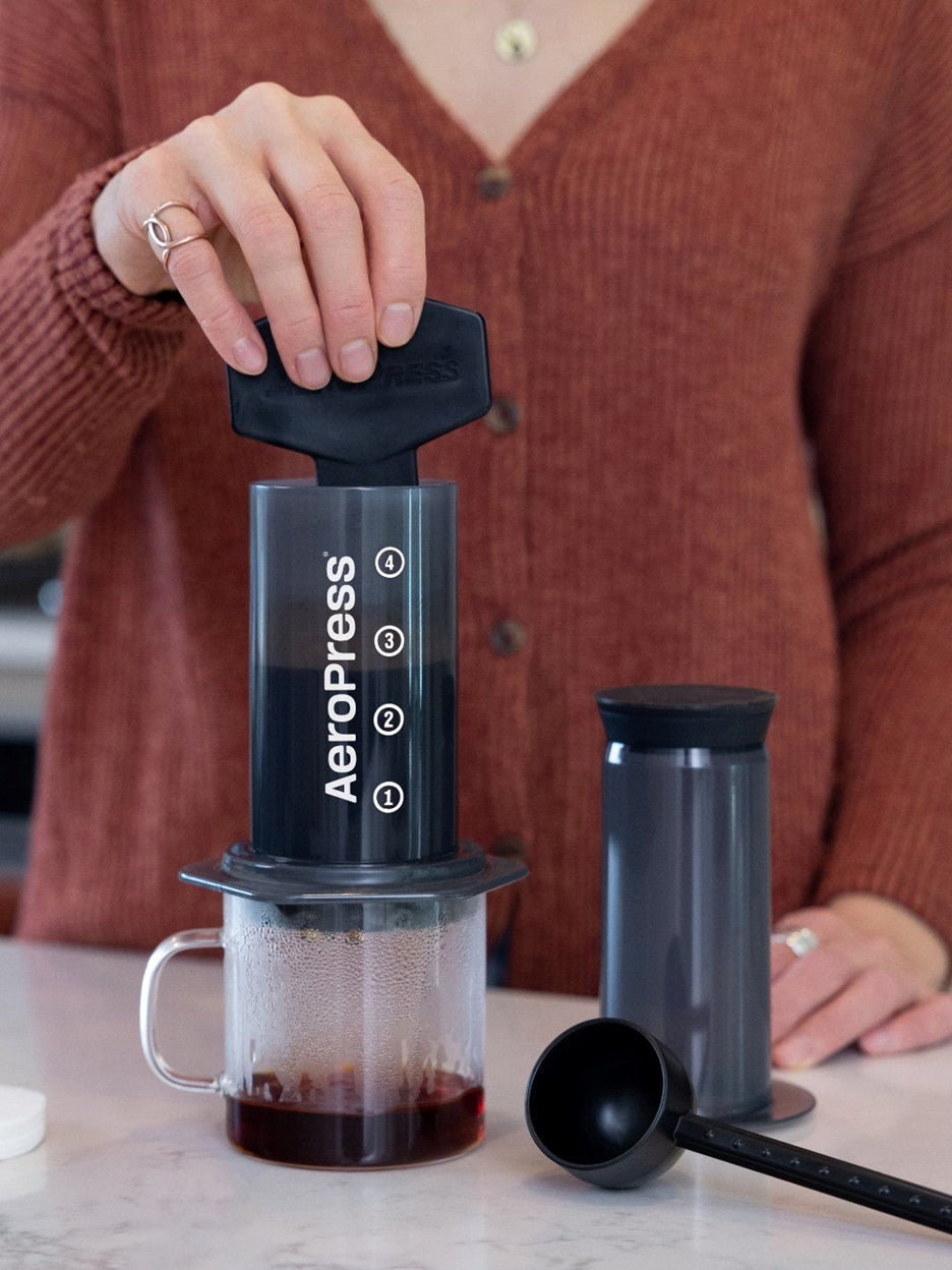 Person using an Aeropress coffee maker on a marble surface