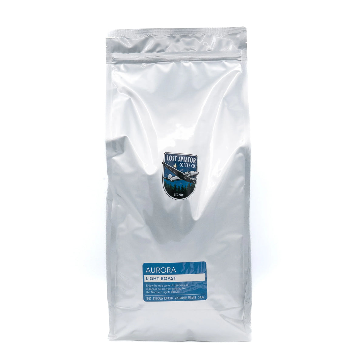 A silver foil bag Aurora Light Roast coffee, featuring a blue and white label near the bottom and a small shield logo in the center, set against a plain white background.