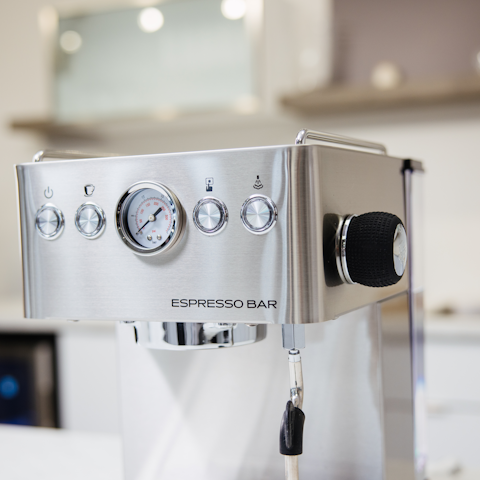 Stainless steel espresso machine with control panel and steam wand in a blurred kitchen setting