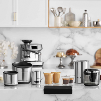 Collection of stainless steel kitchenware on a marble countertop with a coffee machine in the background.