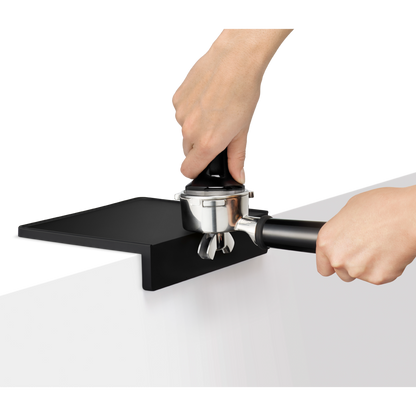 Person using a black and silver coffee tamping device on a white surface