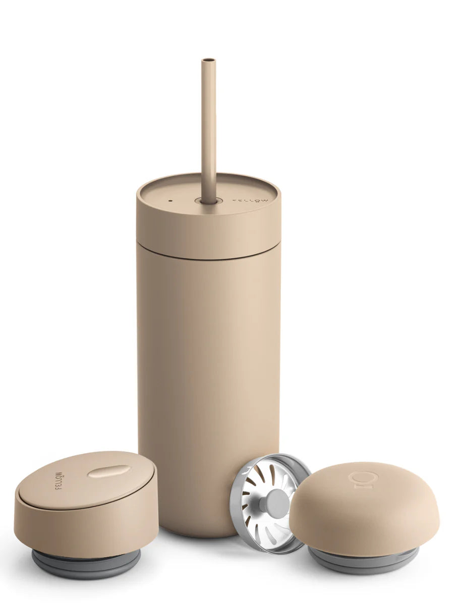 A minimalist travel water bottle with a straw in a matte beige color, shown with its lid and two small accessories on a clean white background.