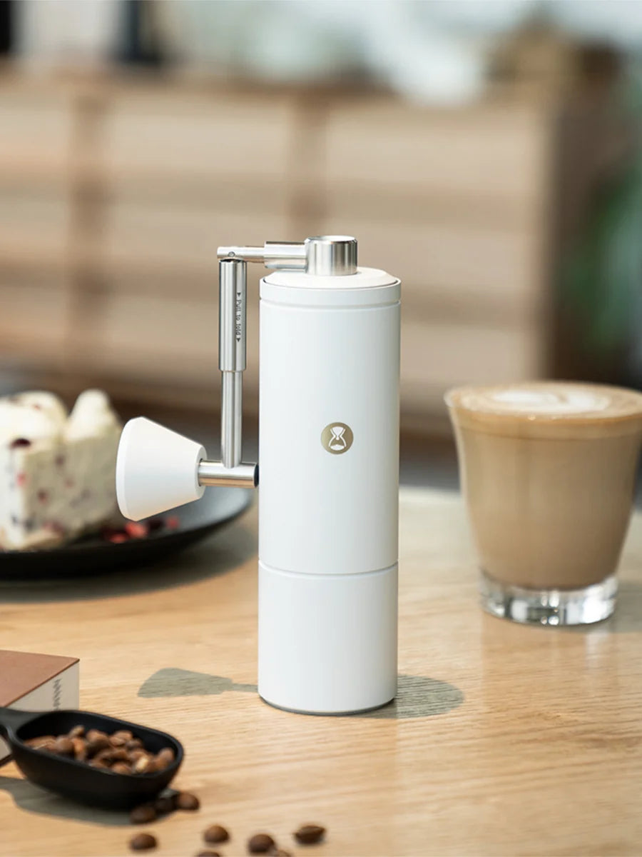 White manual coffee grinder on a wooden table with a blurred background