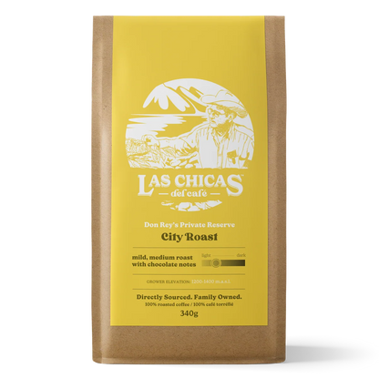 A 340g bag of Las Chicas del Cafe City Roast coffee in a brown kraft paper bag with a bright yellow label, shown against a plain white background.