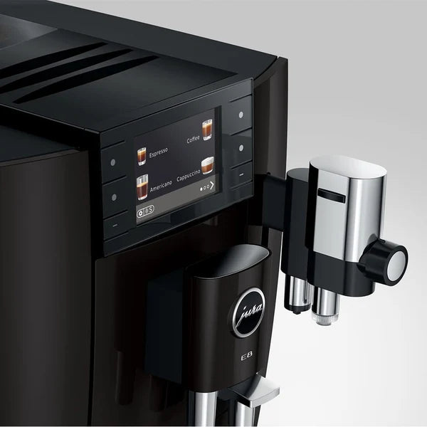 Close-up of a black Jura coffee machine with a digital control panel, drip tray, and a stainless steel steam wand attachment on a light gray background.