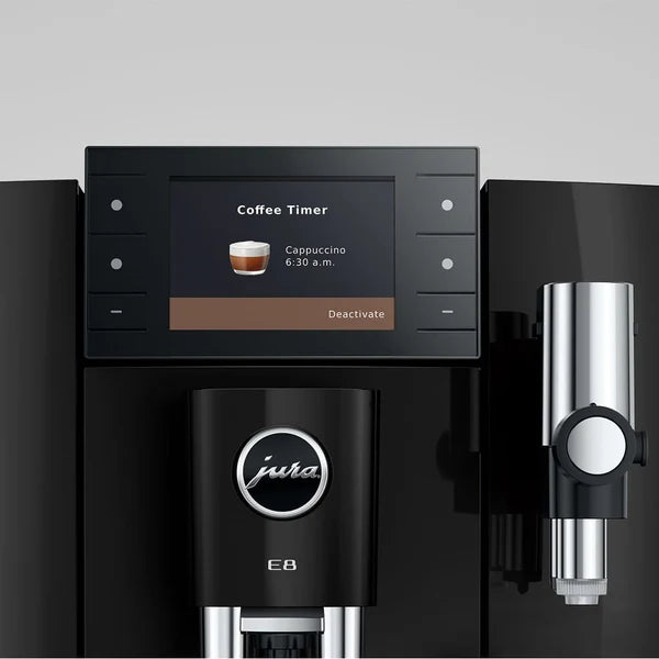 A close-up of a black Jura coffee machine with a digital display screen showing a coffee timer message, a central portafilter holder, and a metallic steam wand attachment on the right, set against a neutral gray background.
