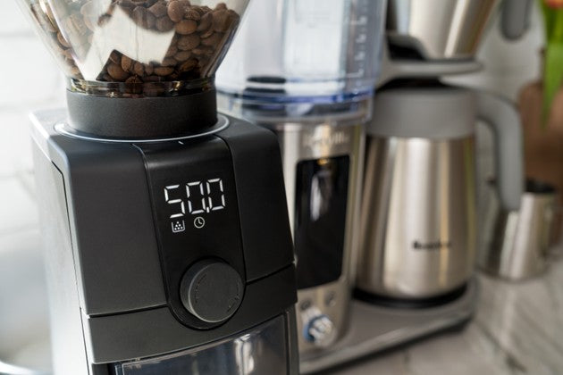 Baratza Coffee grinder with coffee beans and a coffee maker in the background