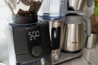 Baratza Coffee grinder with coffee beans and a coffee maker in the background