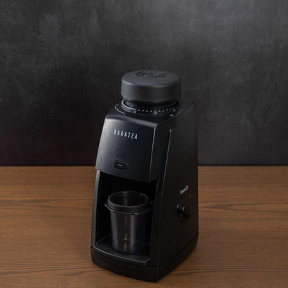 Black coffee maker with a cup on a wooden table against a dark background