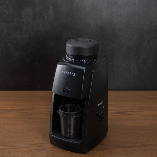 Black coffee maker with a cup on a wooden table against a dark background