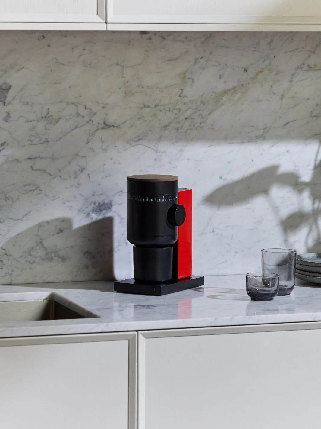 A black and red modern coffee grinder in a white marble modern kitchen.
