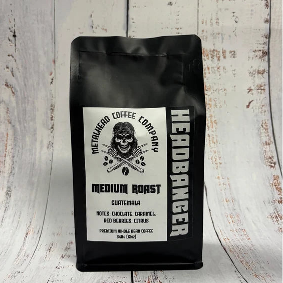 A black bag of Metalhead Coffee Company Headbanger Medium Roast coffee stands upright on a whitewashed wooden surface.