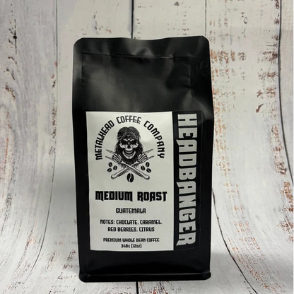 A black bag of Metalhead Coffee Company Headbanger Medium Roast coffee stands upright on a whitewashed wooden surface.