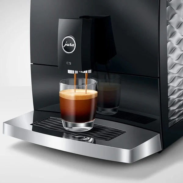A black and silver Jura coffee machine dispensing espresso into a glass cup on a white background.