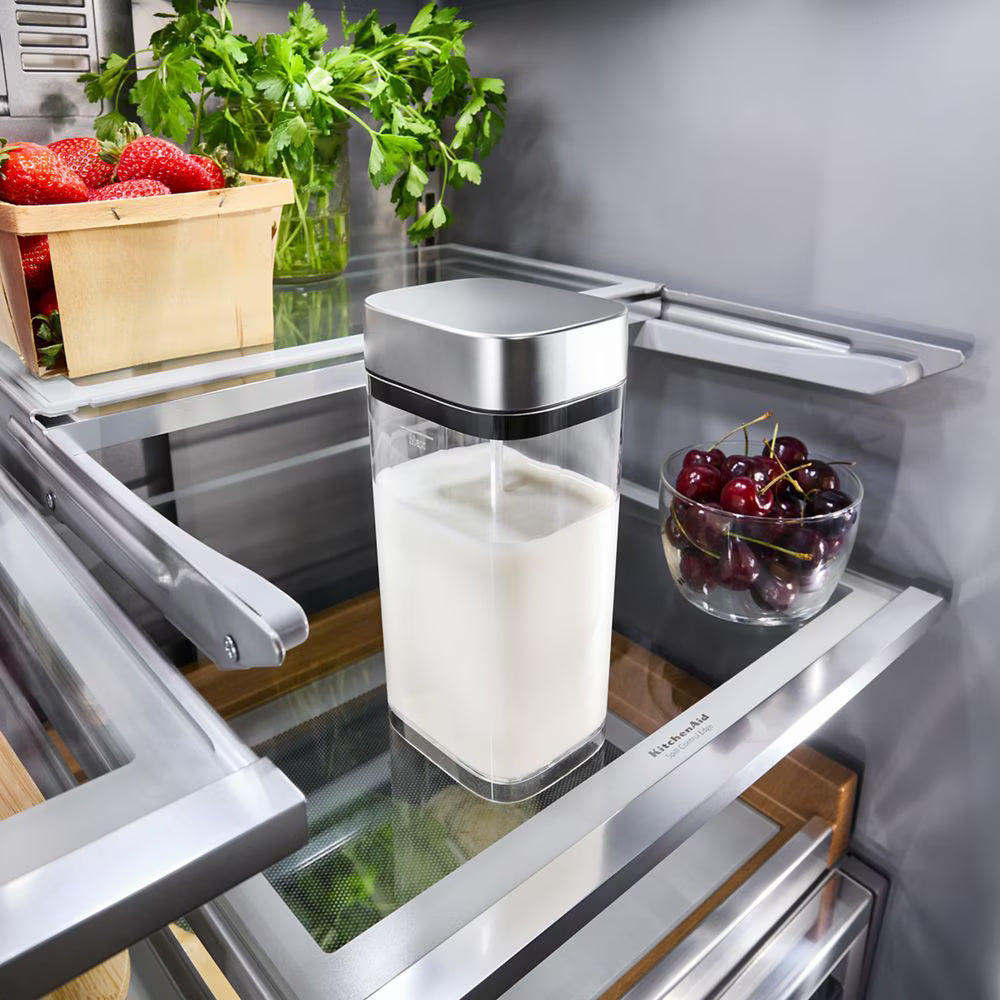 Open refrigerator with a container of milk and a bowl of cherries on a shelf.