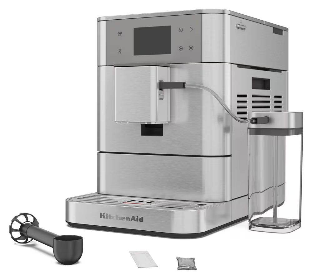 KitchenAid stainless steel automatic espresso machine with a digital display screen, shown with a clear water tank, black milk frother, and two small accessory packets on a white background.