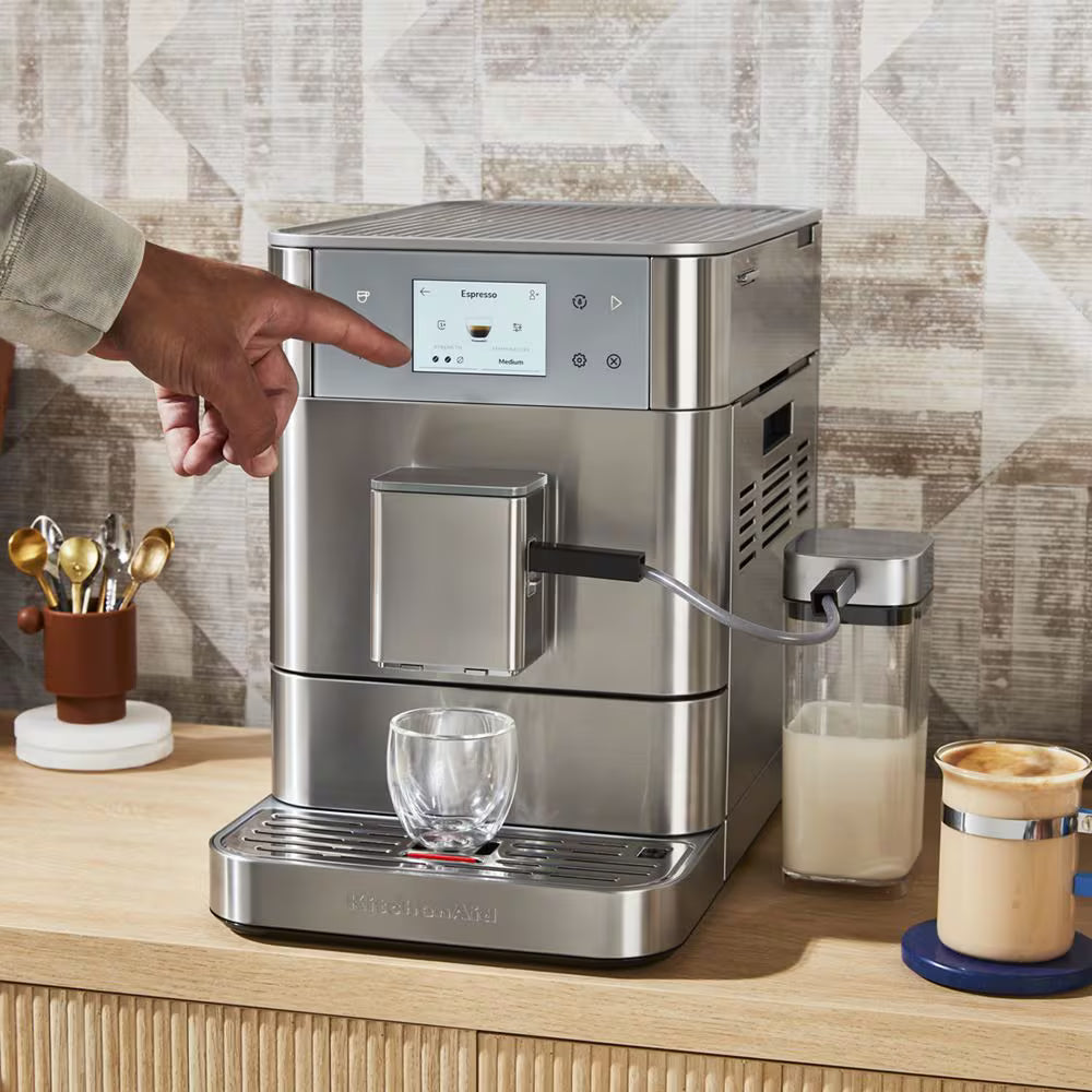 Stainless steel coffee machine on a kitchen counter with a person interacting with it.