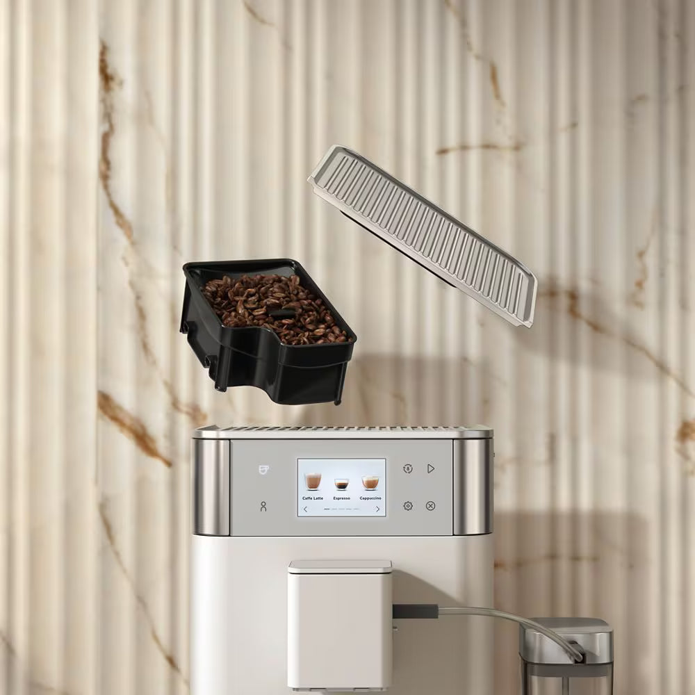 A modern coffee machine with a digital control panel, shown with a black bean hopper filled with coffee beans floating above it and a slotted lid component above, set against a beige marble-look wall background.