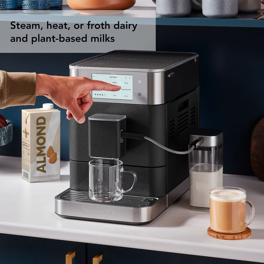 Coffee machine being used to prepare a drink on a kitchen counter with almond milk carton and glass of coffee.