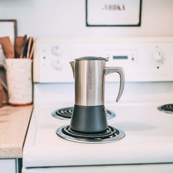 Stainless steel espresso maker on a stovetop with a blurred kitchen background