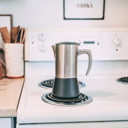 Stainless steel espresso maker on a stovetop with a blurred kitchen background