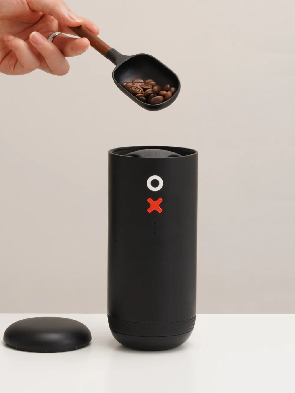 Black coffee grinder with a scoop of coffee beans on a neutral background