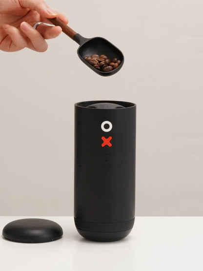 Black coffee grinder with a scoop of coffee beans on a neutral background