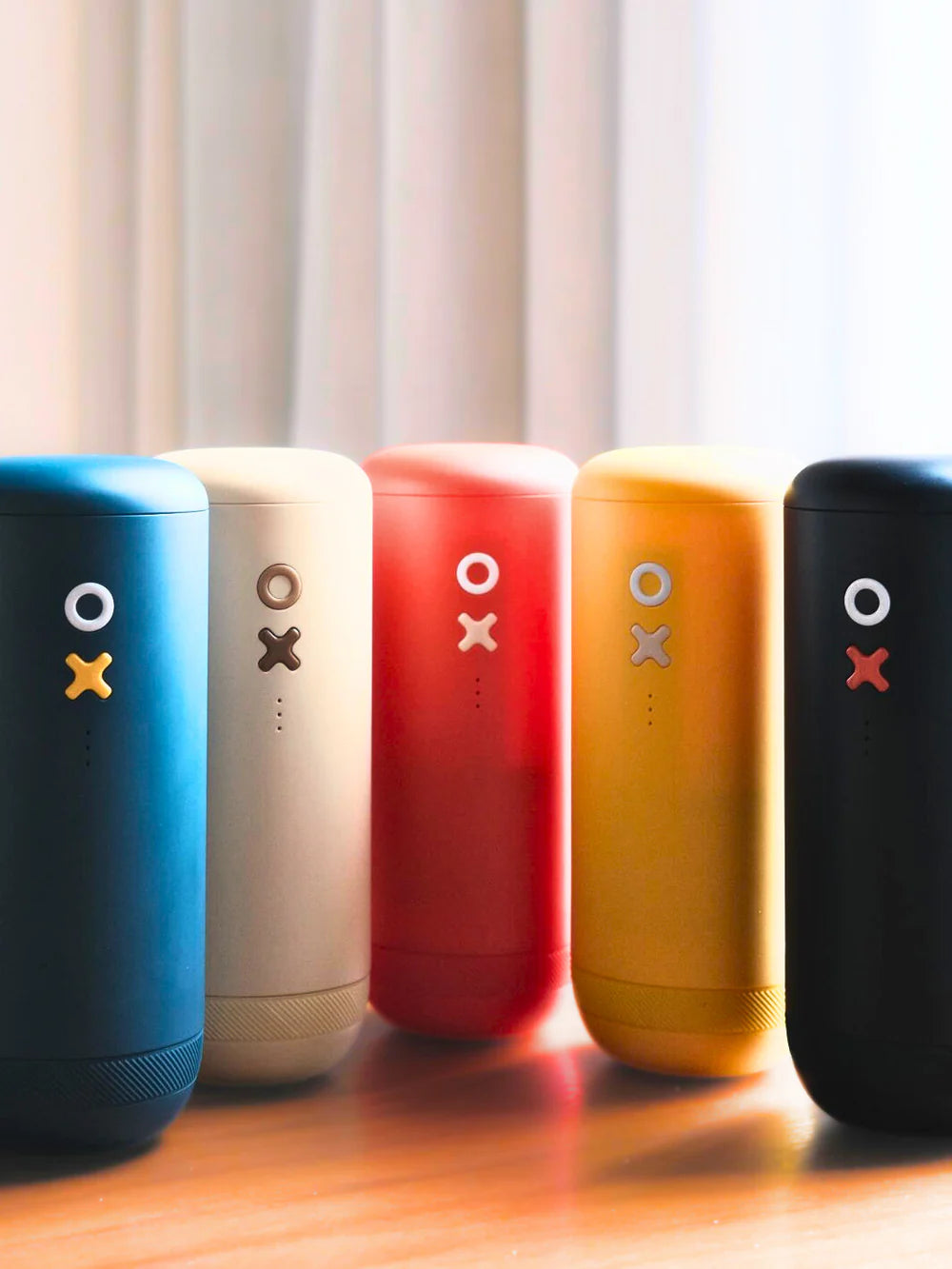 Five colorful cylindrical portable coffee grinders with OX designs on a wooden surface.