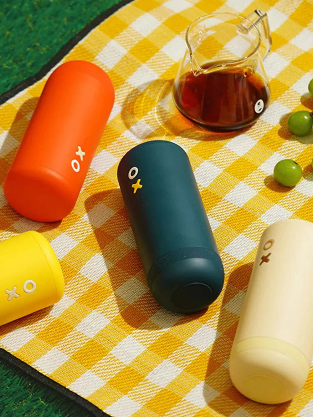 Four cylindrical colourful portable coffee grinders on a yellow checkered tablecloth.