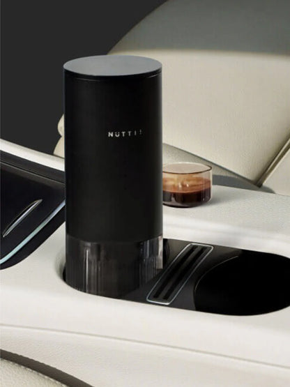 Black NUTTII device in a car cup holder with a glass of coffee in the background