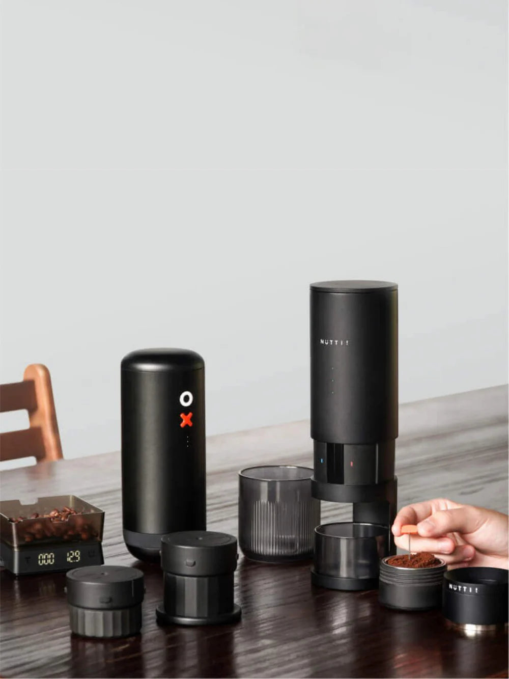 Black coffee brewing device on a table with glasses and a wooden chair.