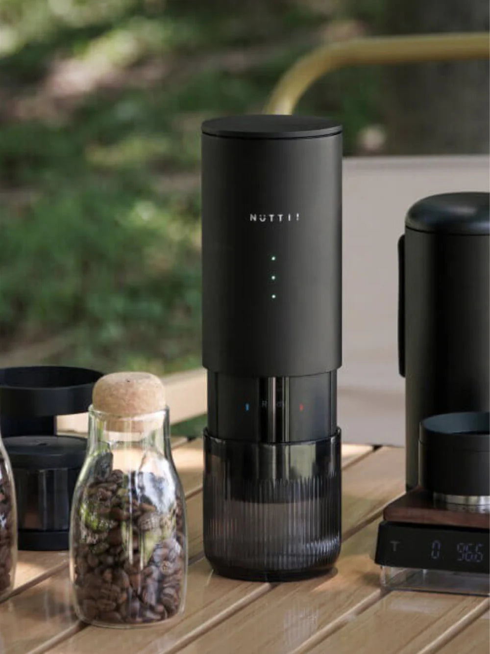 Black espresso machine on a wooden surface with coffee beans and a bottle in the background.