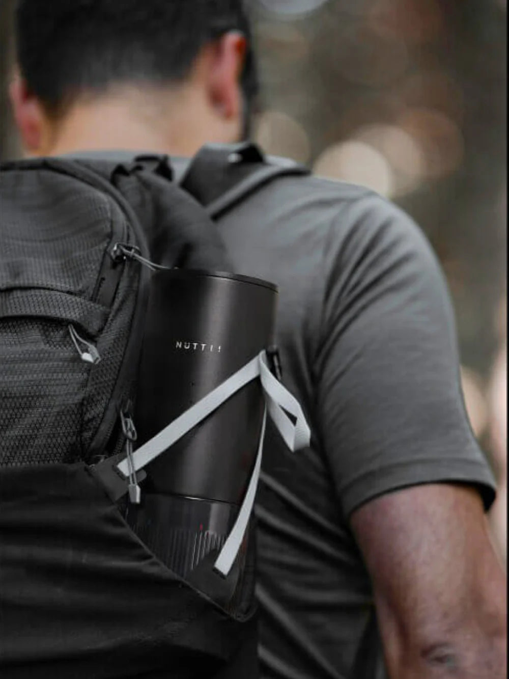 Person wearing a black backpack with a compact Nuttii branded espresso machine in the side pocket.