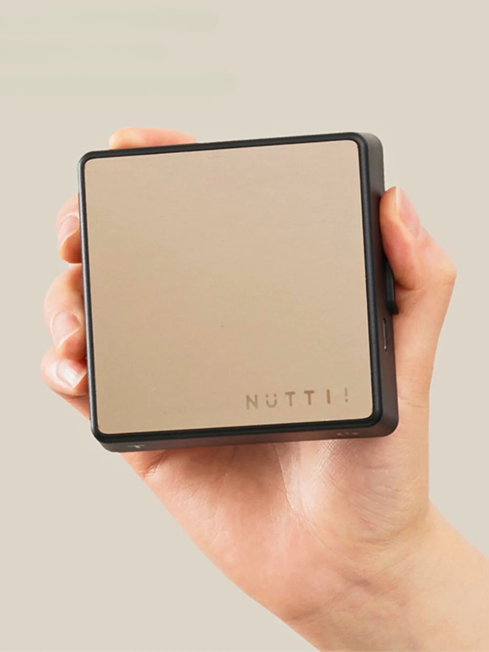 Hand holding a compact coffee scale with 'NUTTII' branding against a neutral background