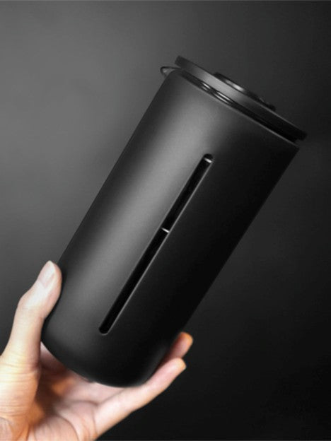 Black cylindrical container held in a hand against a dark background