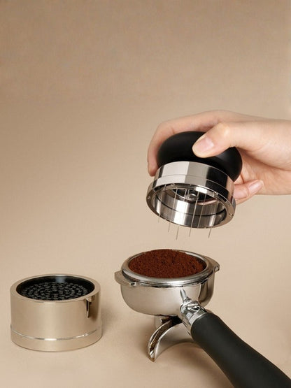 Hand holding a needle distribution tool near a portafilter with ground espresso beans on a beige background