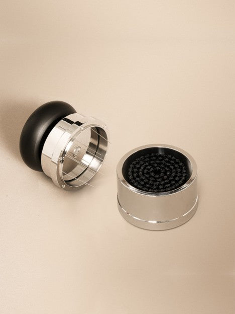 Coffee distribution tool next to black and metal base, on a beige background