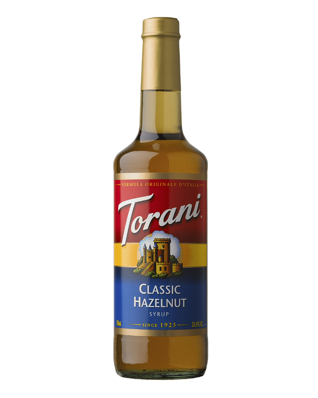 A bottle of Torani Classic Hazelnut Syrup on a plain white background. The bottle is filled with golden-brown syrup and features a label with red, yellow, and blue sections, and the brand name 'Torani' in white script.