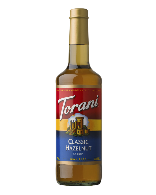 A bottle of Torani Classic Hazelnut Syrup on a plain white background. The bottle is filled with golden-brown syrup and features a label with red, yellow, and blue sections, and the brand name 'Torani' in white script.