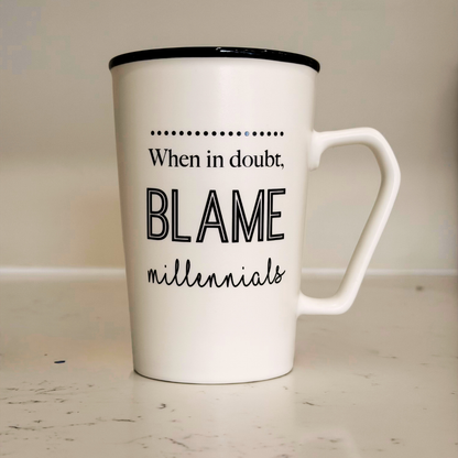 White mug with black text 'When in doubt, blame millennials' on a light wooden surface.