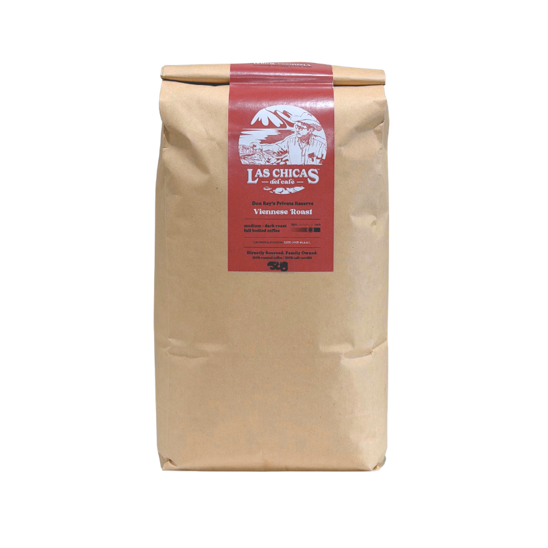 A brown kraft paper bag of Las Chicas Coffee Roasters, featuring a red label with white text and graphics, set against a plain white background.