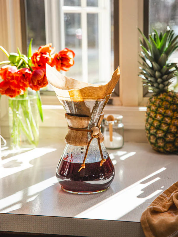 Chemex coffee maker with coffee on a kitchen counter with flowers and a pineapple in the background